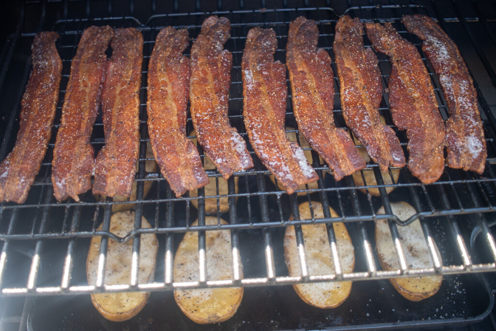 crispy bacon slices on a rack over potato halves on the smoker