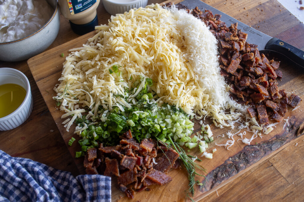shredded cheeses, chopped bacon, green onions on a wooden board - prep for filling