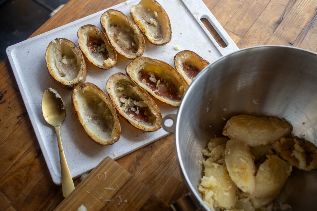 hollowed out cooked potatoe halves and a bowl with the potatoe flesh in