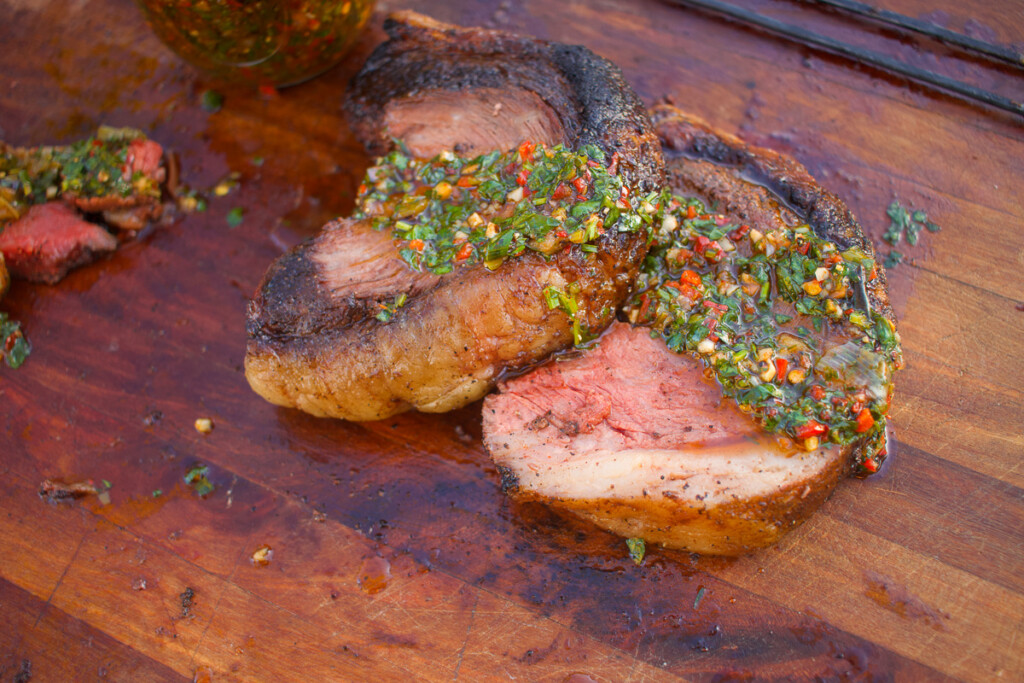 slices of picanha steak on a wooden board with chimichurri drizzled over them