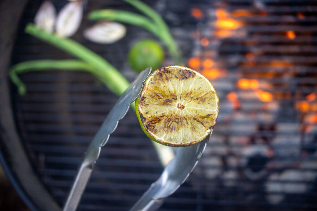 a pair of tongs holding onto a grilled lime.