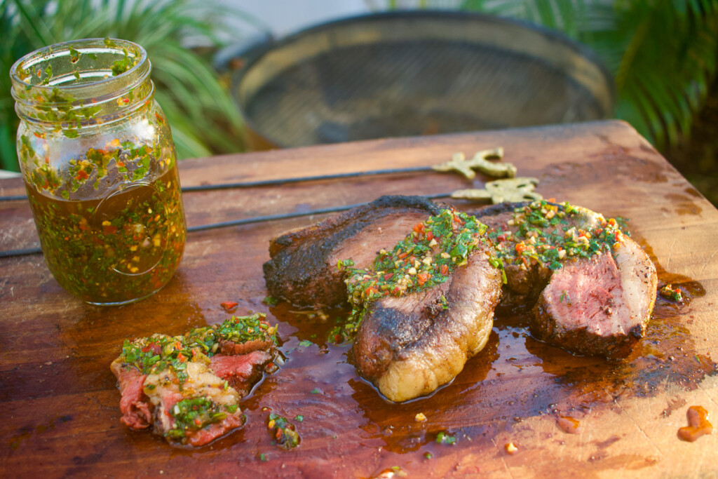 picanha steak sliced, on a wooden board with chimichurri drizzled over it.