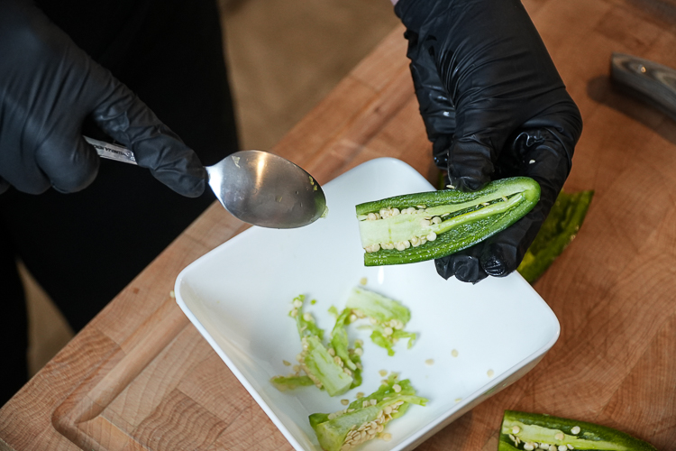 scraping seeds out of a jalapeno half with a spoon