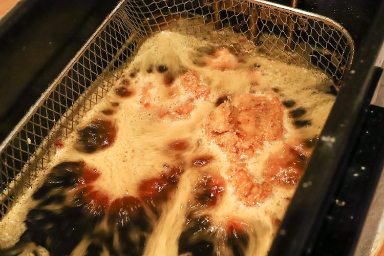 fryer basket with chicken thighs submerged in oil