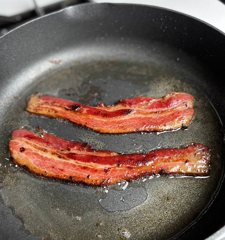 two strips of bacon frying in a pan