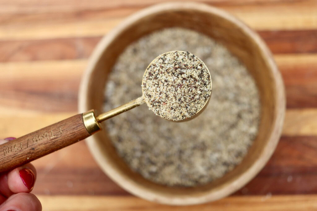 a spoonful of steak seasoning with a bowl of seasoning in the background