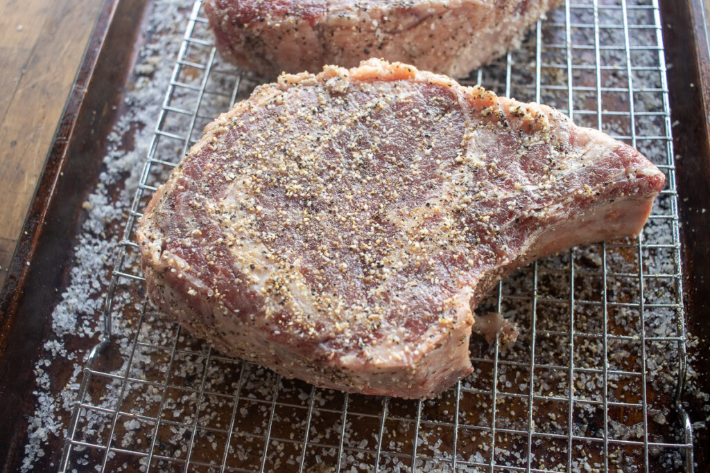 a raw rib eye steak on a wire rack sprinkled with steak seasoning