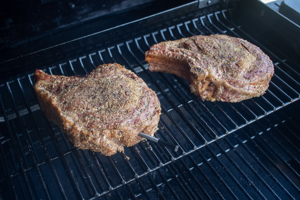 two cooked rib eye steaks on the top rack of the smoker