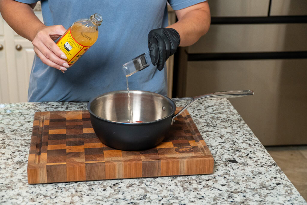 a hand measuring out apple cider vinegar into a metal bowl