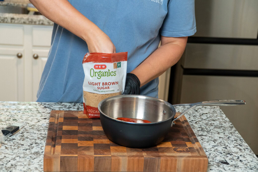 a person reaching into a  bag of brown sugar to add to a metal bowl