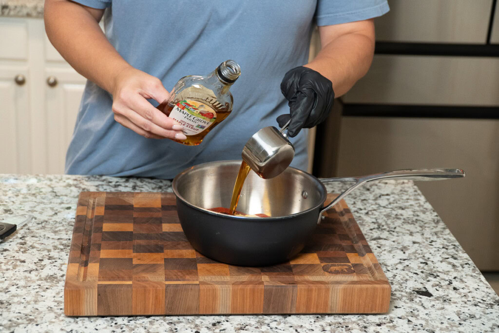 a person measuring maple syrup into a metal bowl