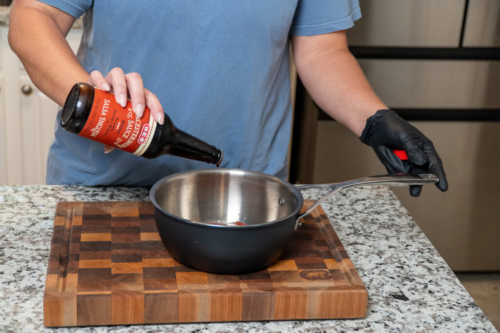 a person holding a bottle of Worcestershire sauce tipping some into a metal bowl