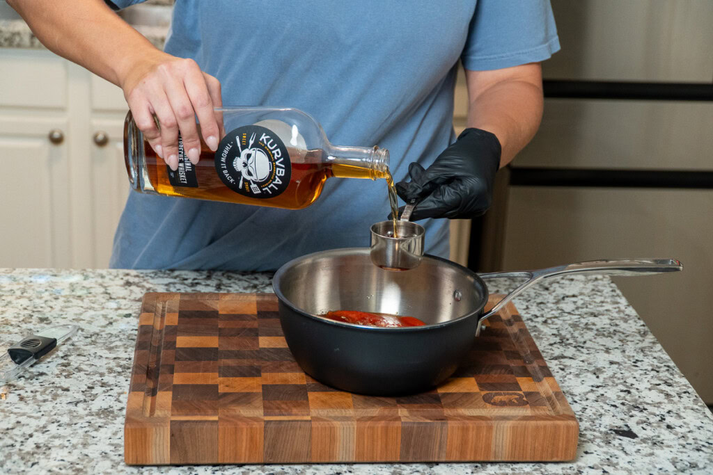 a person measuring bourbon into a measuring cup to add to a metal bowl