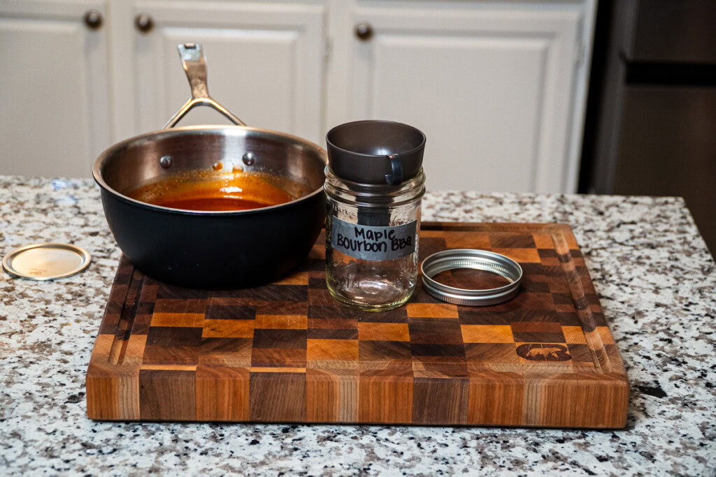 a pot of suace and an jar ready for it to be poured into sitting on a wooden board