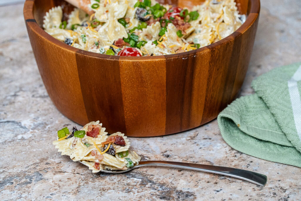 creamy bacon ranch pasta salad in a wooden bowl with a spoonful in front of it