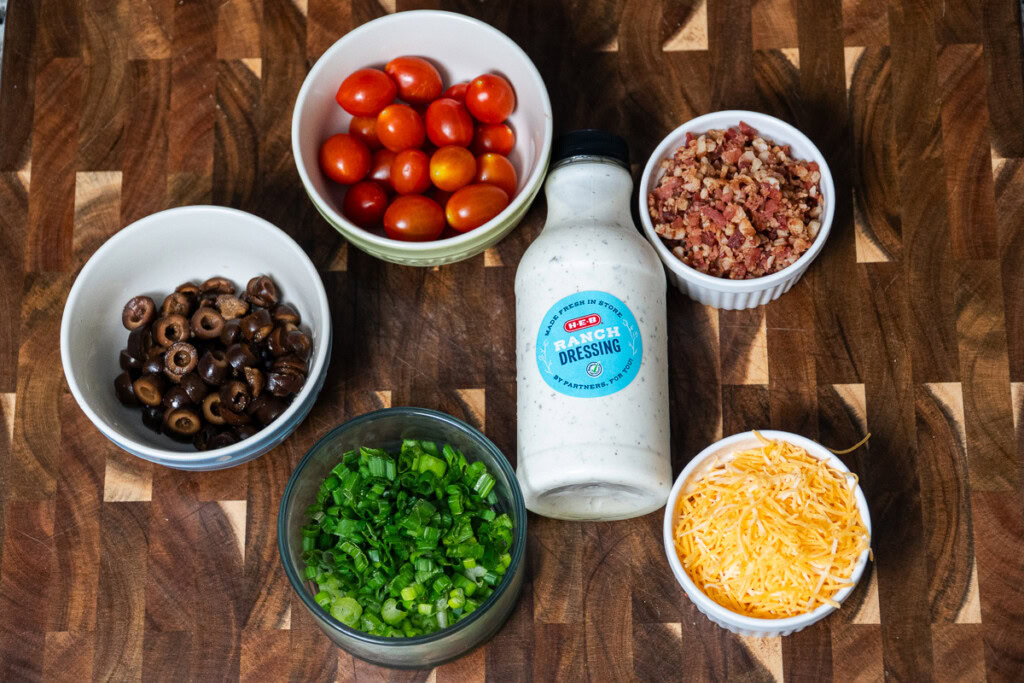 all the ingredients for the pasta salad laid out on a wooden chopping board