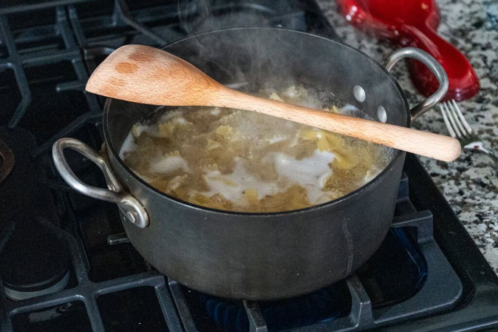 a black pot of the burner filled water water and pasta with a wooden spoon resting on top