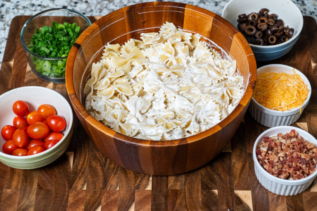a large wooden bowl with cooked farfalle past in it covered in ranch dressing