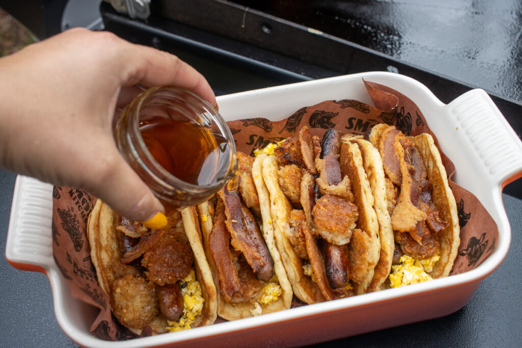 a hand pouring maple syrup over pancake breakfast tacos