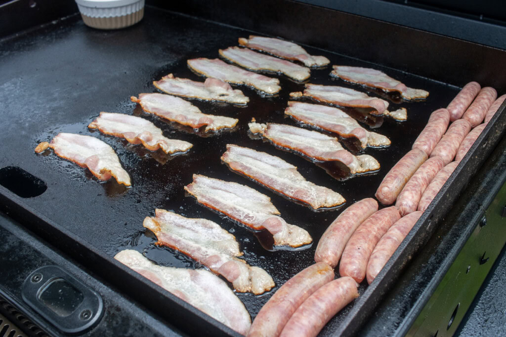 raw bacon and sausages on the griddle