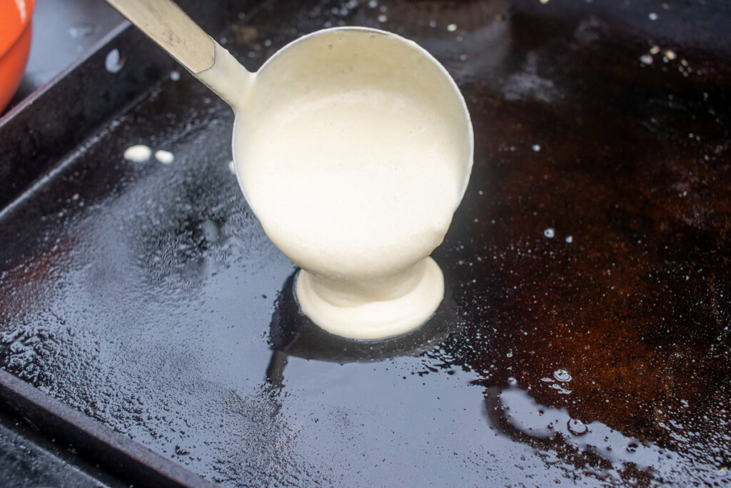 a ladle pouring pancake batter onto a hot griddle