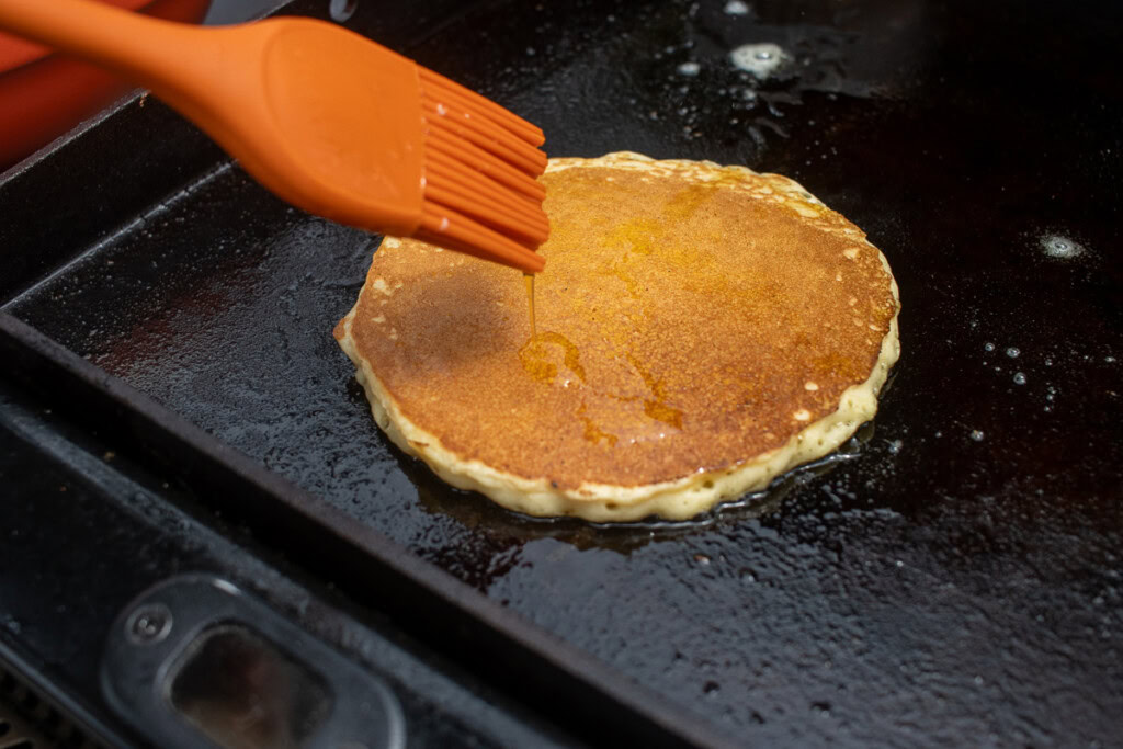 a pancake on the griddle being brushed with butter