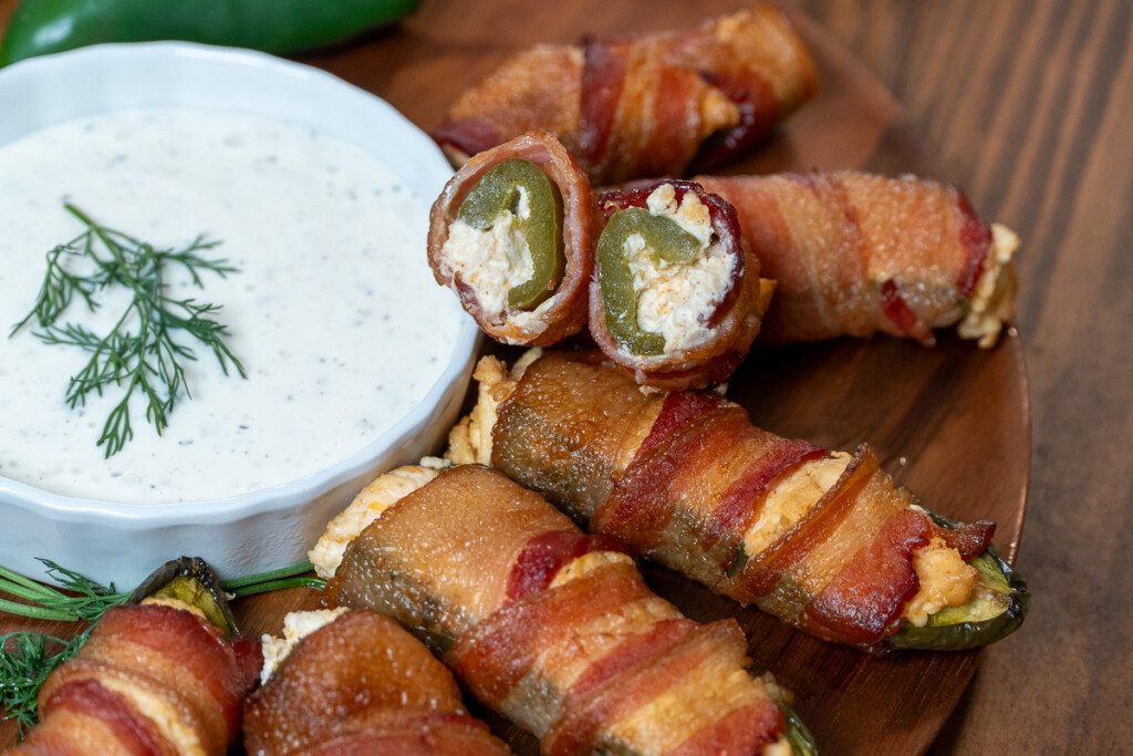 a bowl of dip and jalapeno poppers on a board