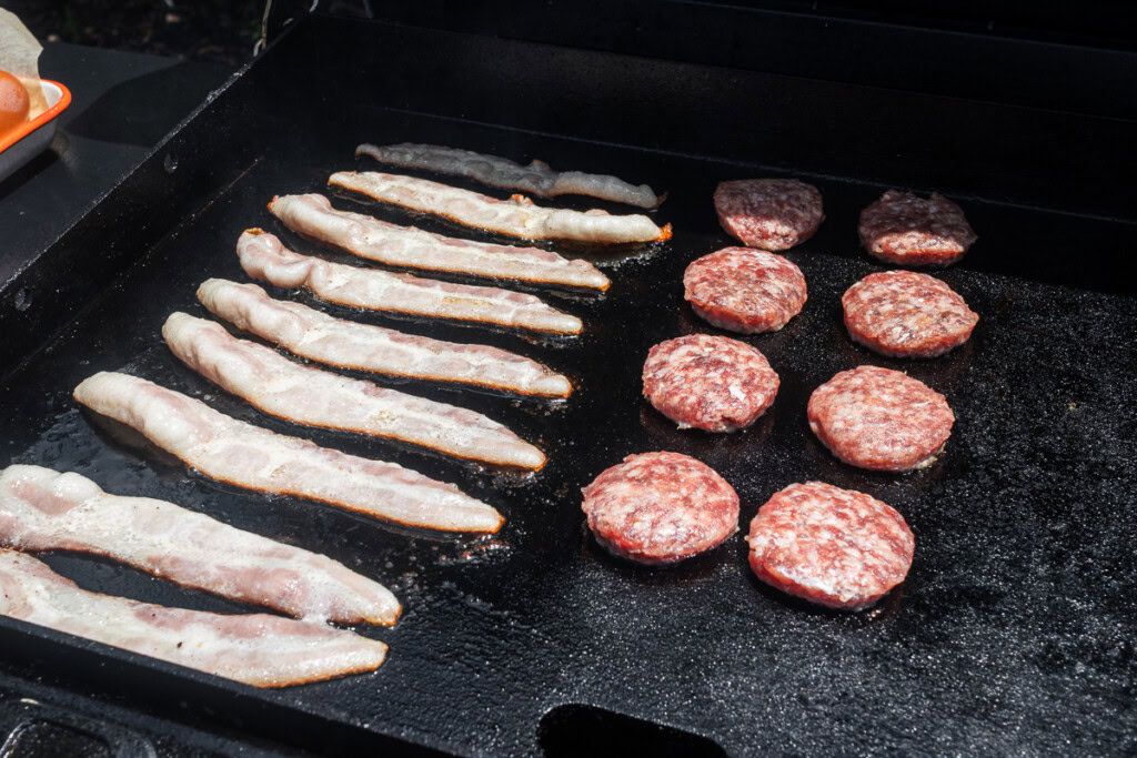 raw bacon and sausage cooking on the griddle