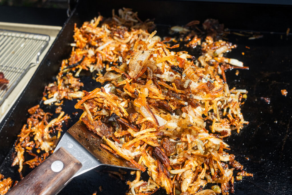 a spatula underneath the hash brown cooking on the griddle