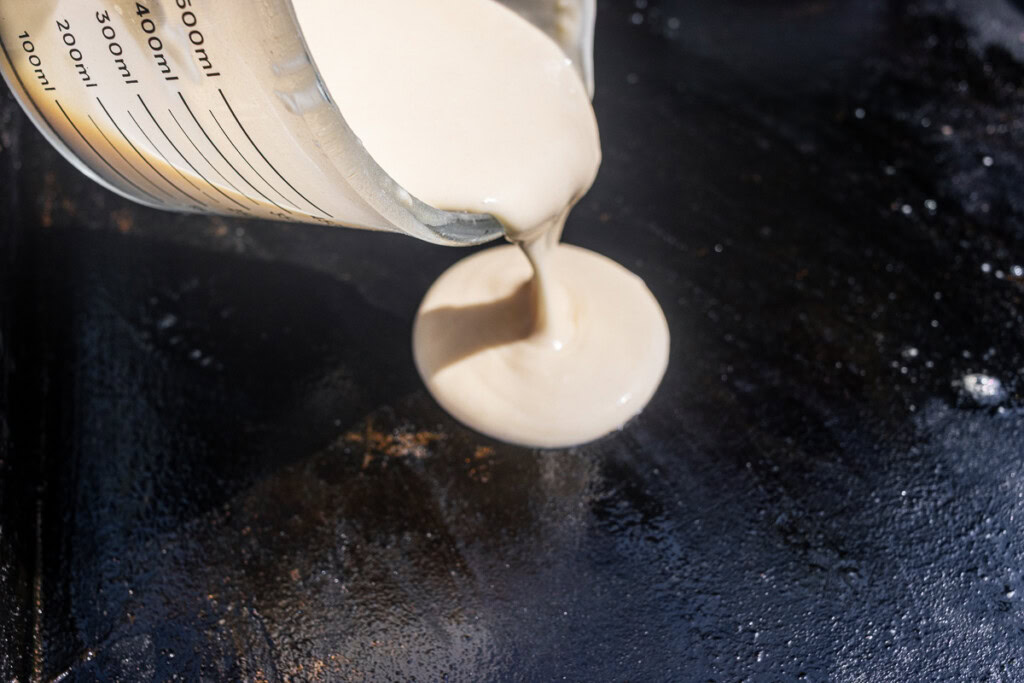 a jug with pancake mixture being poured onto the griddle