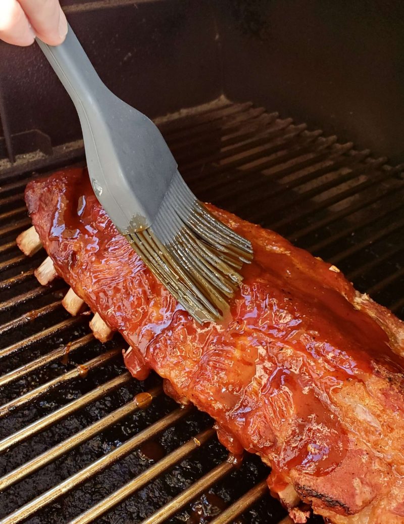 Saucing BBQ pork ribs with BBQ sauce and a basting brush