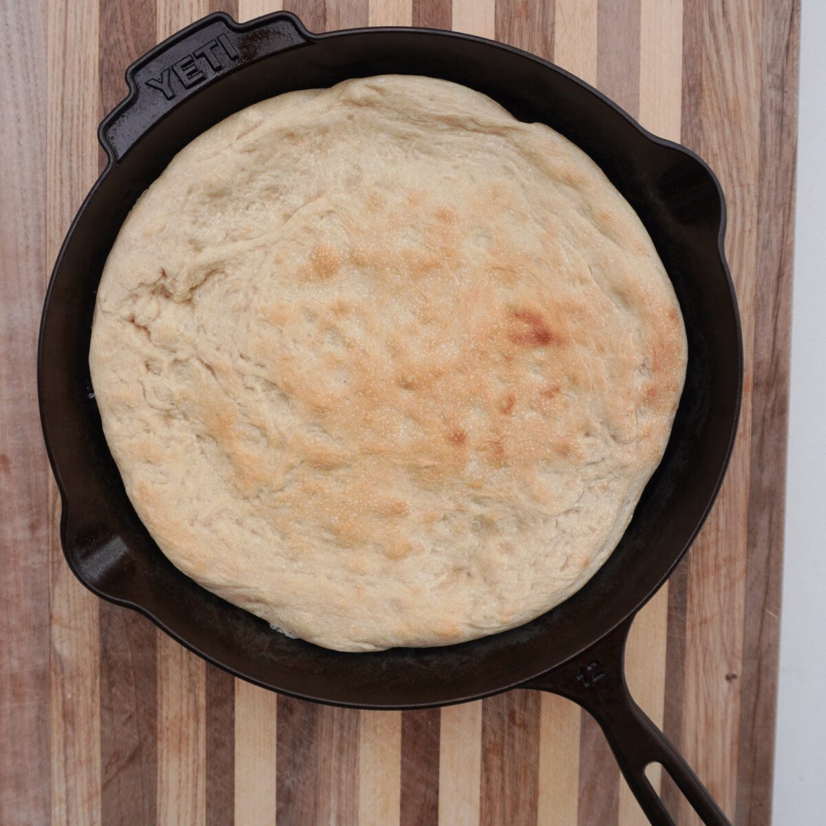 pre-baked pizza dough in yeti cast iron skillet on a cutting board.