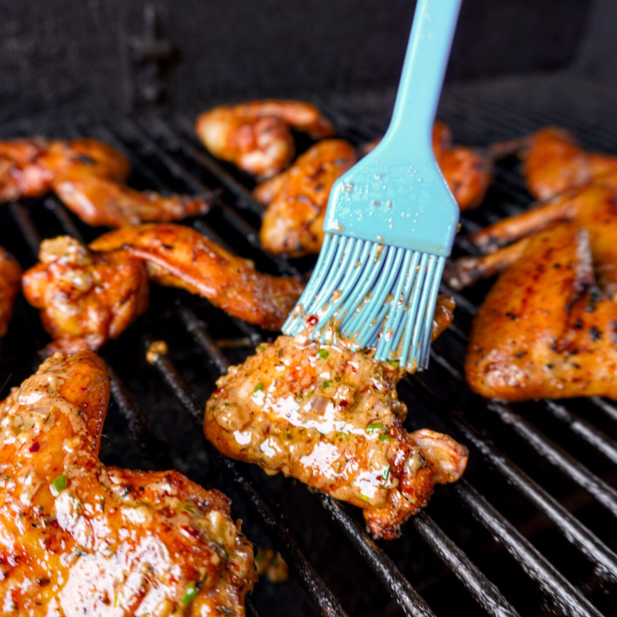 cowboy butter sauce being brushed on chicken wings while on the grill.