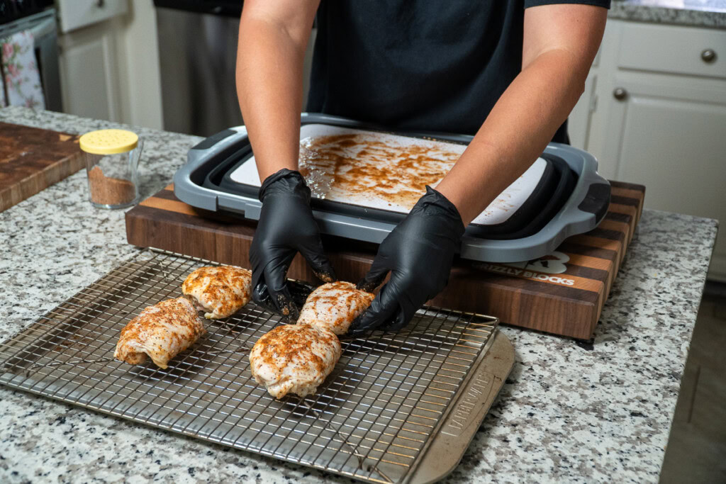 raw seasoned chicken thighs being placed on a wire rack