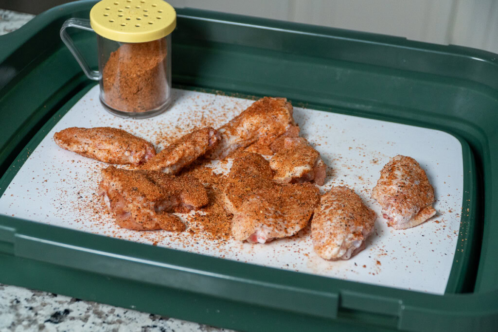 raw chicken wings on a white board sprinkled with BBQ seasoning