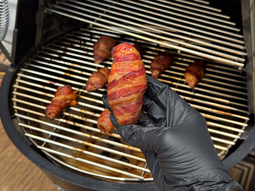 a black gloved hand holding a cooked bacon wrapped chicken wing