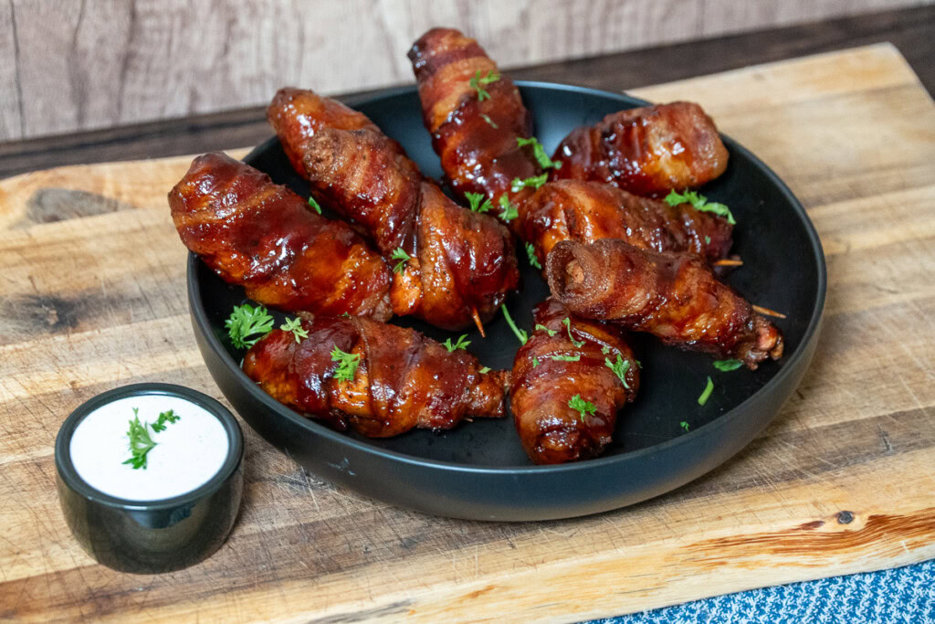 smoked bacon wrapped chicken wings on a black plate with a bowl of ranch dressing alonside
