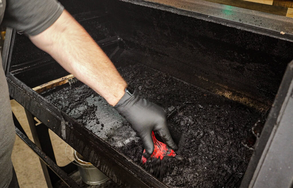Scraping heavy grease and carbon buildup from inside a dirty pellet grill using a red plastic scraper and black nitrile gloves