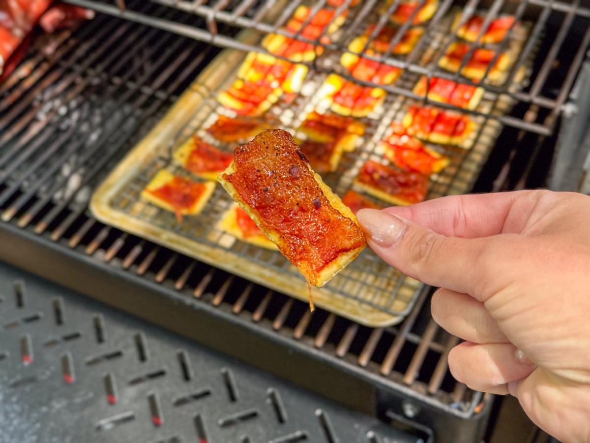 a hand holding a smoked billionaire bacon cracker