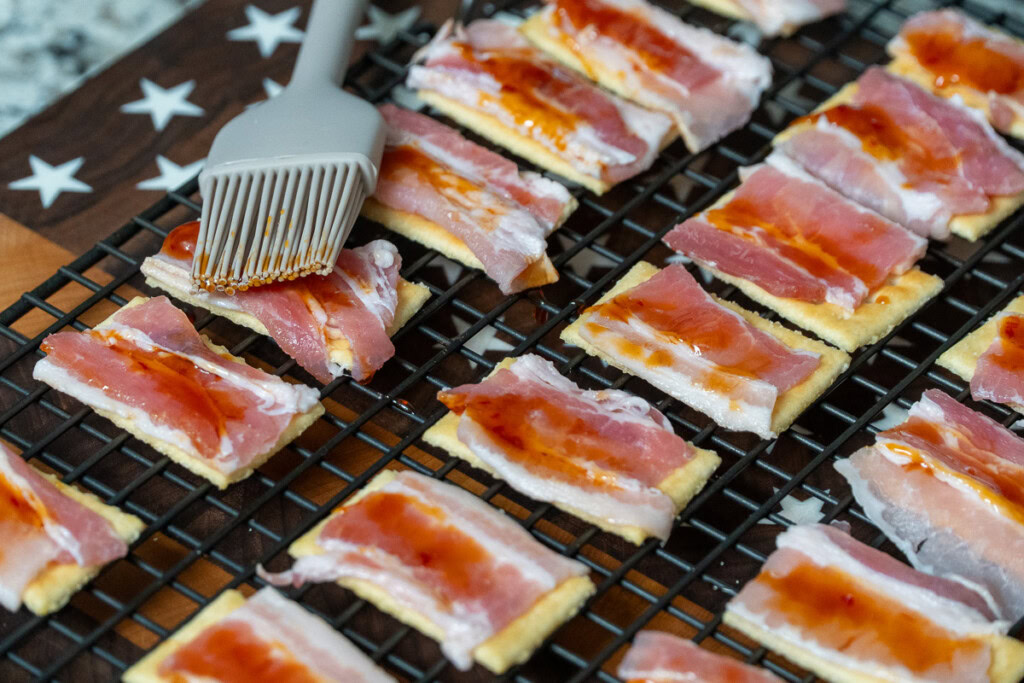 a basting brush spreading hot honey on the bacon topped crackers