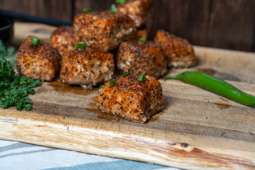 cooked smoked salmon burnt ends on a wooden board with some green onions