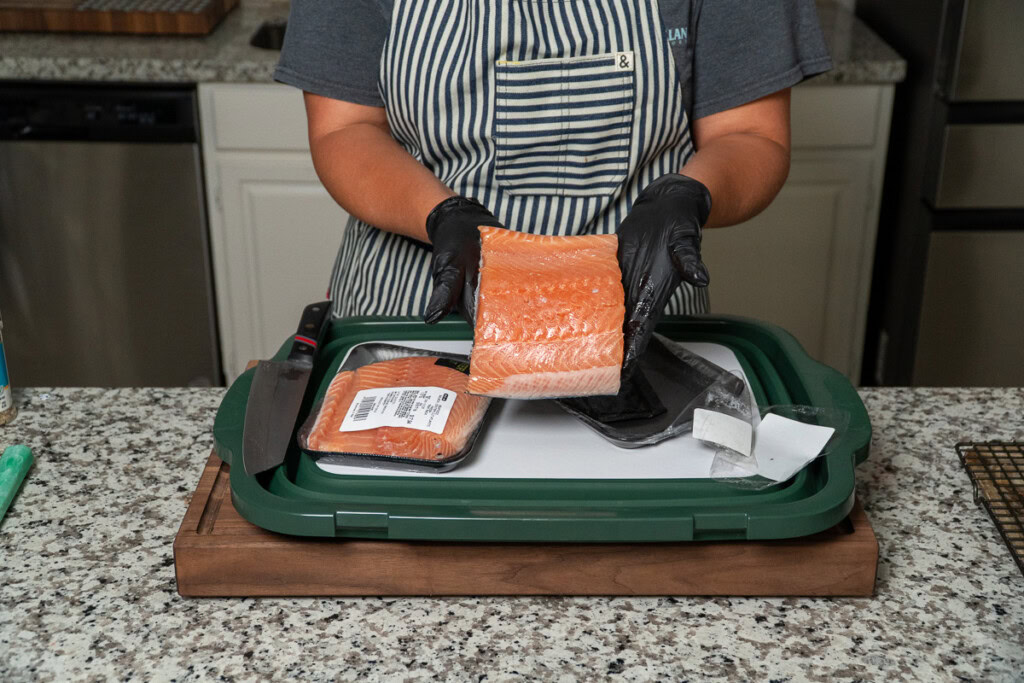 a person holding a piece of raw salmon with the flesh side facing