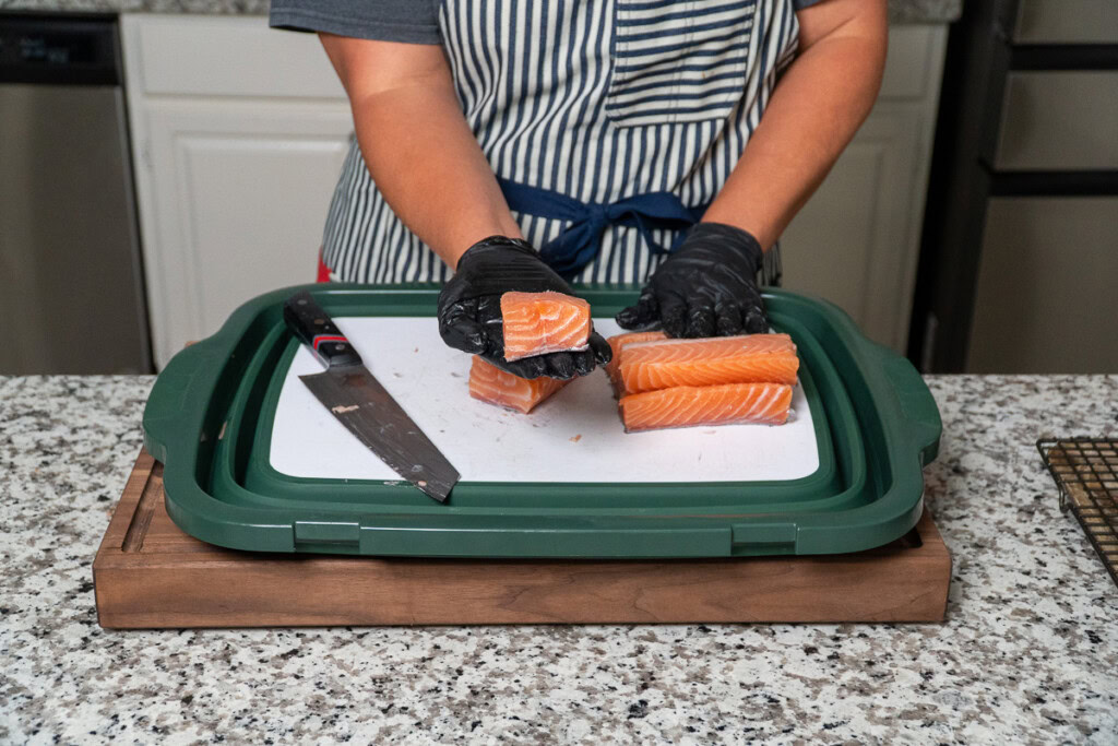 a person is holding up a cube of raw salmon they have cut