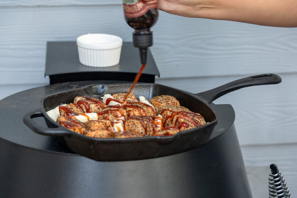 Hot honey being drizzled over a cast iron pan of salmon cubes