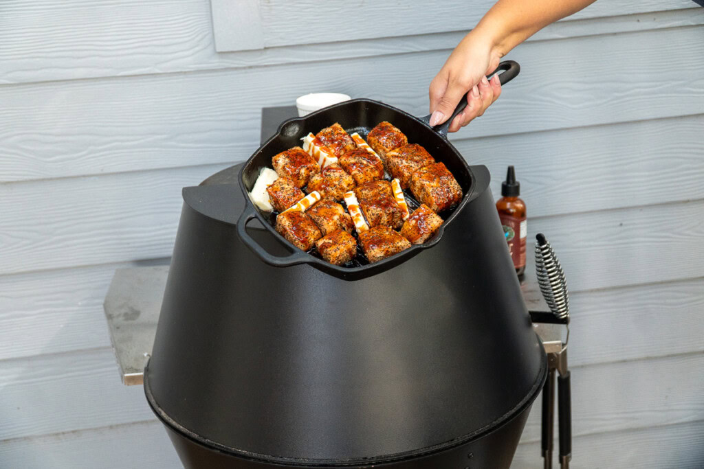 A cast iron pan of salmon cubes with butter pats and hot honey drizzled over them