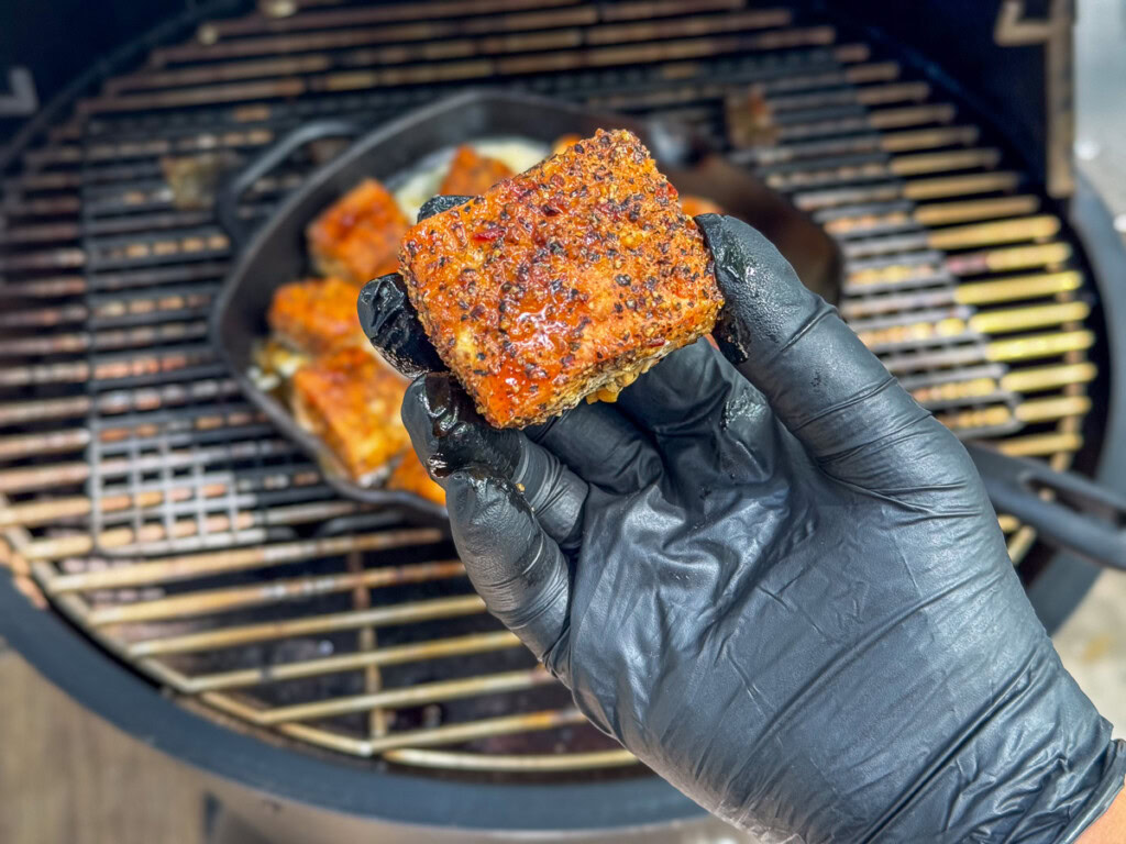 a black gloved hand holding a cooked smoked salmon burnt end