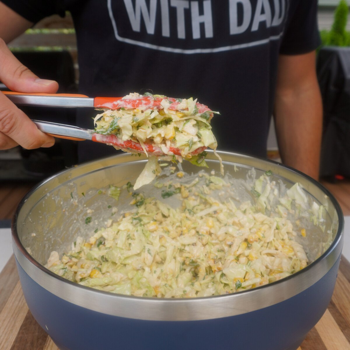 corn slaw mixed together in yeti bowl. Tongs showcasing a batch above the bowl for the grilled shrimp with corn slaw tacos.