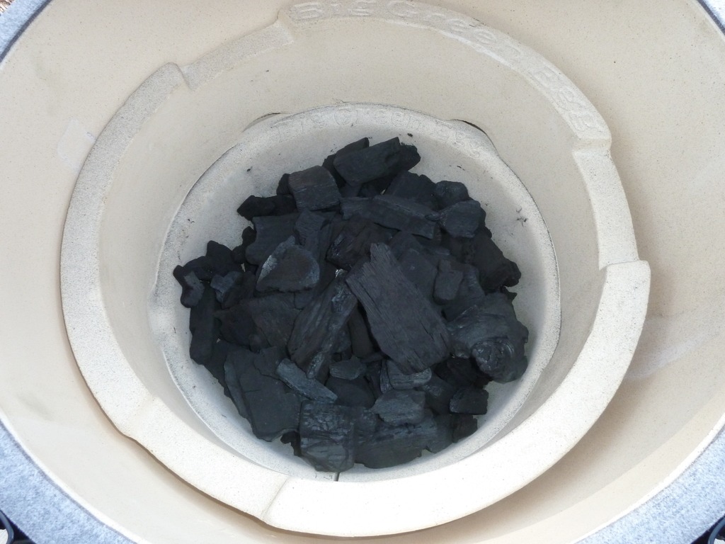 A close-up view of a ceramic grill or kamado, such as the Big Green Egg, filled with irregular pieces of black charcoal—ready for lighting and grilling. Perfect for those learning how to light a Big Green Egg.