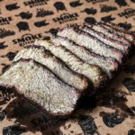 Slices of smoked chuck roast on butcher paper, showing juicy brisket-style texture, dark bark, and a red smoke ring.