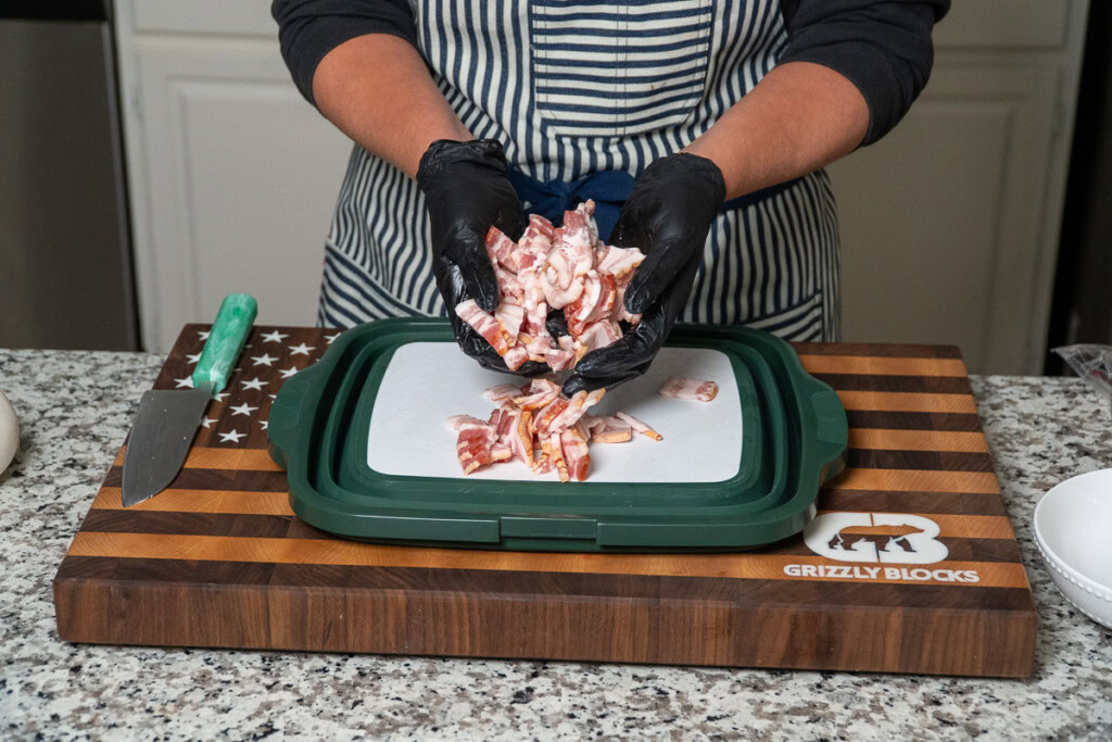 a person with black gloves on holding up sliced bacon
